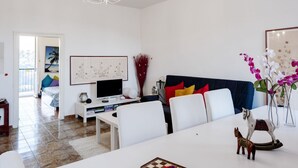 Una sala de estar moderna con una mesa de comedor, sofás blancos, un televisor y una araña.