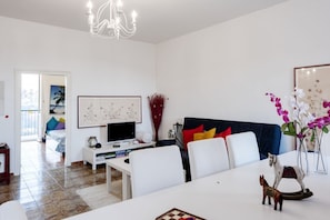 Una sala de estar moderna con una mesa de comedor, sofás blancos, un televisor y una araña.