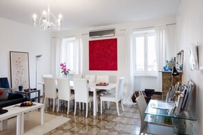 Ein modernes Wohnzimmer mit Essbereich, weißen Möbeln, einem Kronleuchter und einer roten Akzentwand.
