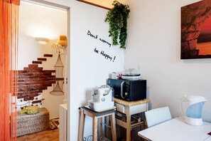 Eine Küche mit Mikrowelle, Toaster und Wasserkocher auf einem Holztisch, einer Ziegelwand und einer hängenden Pflanze.