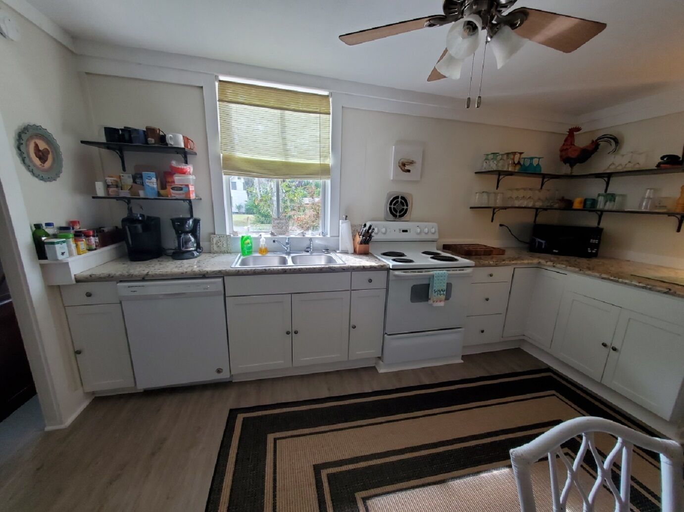 A kitchen with white cabinets, a stove, a sink, and a ceiling fan.