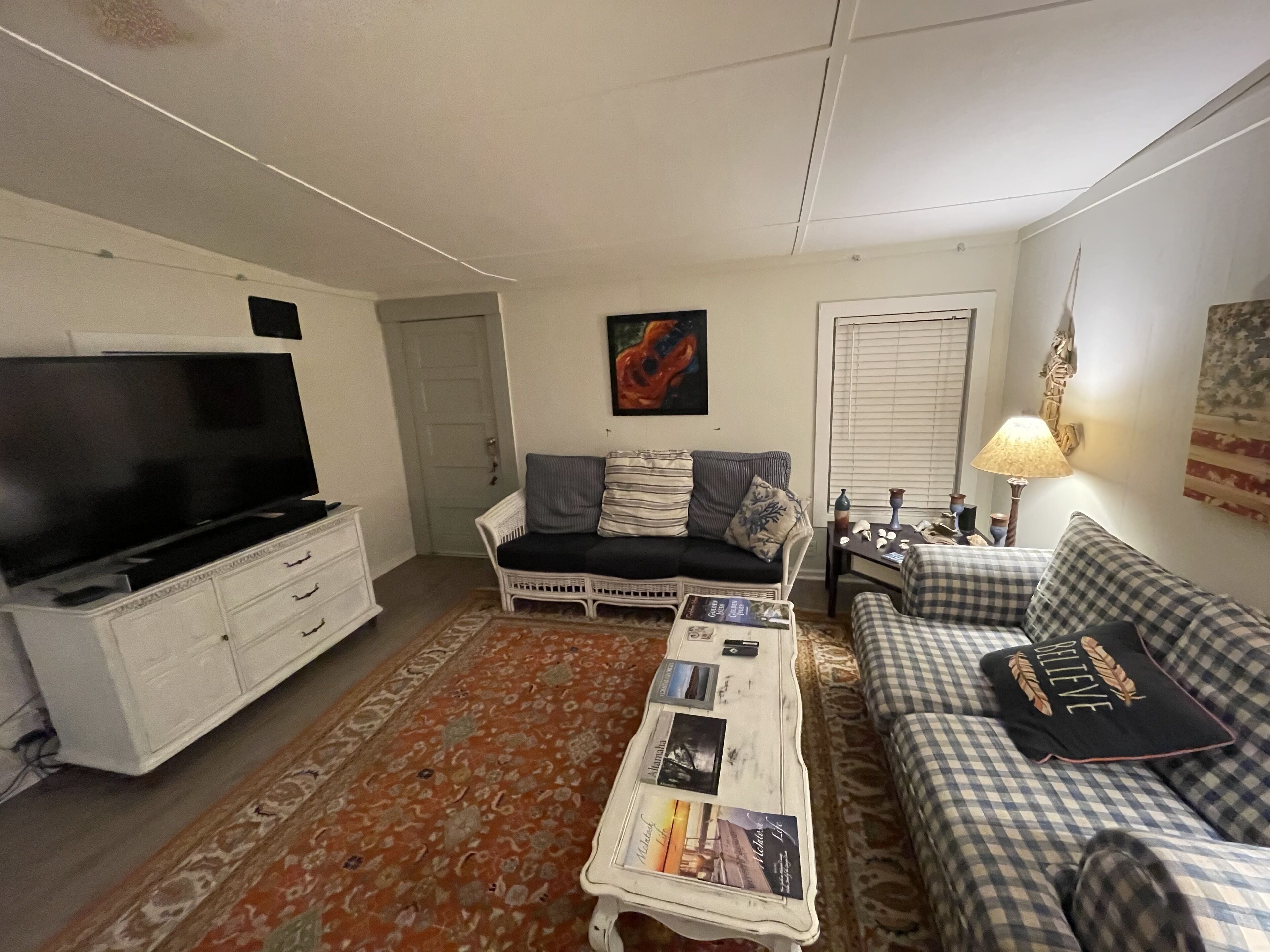 A living room with a flat-screen TV, two sofas, a coffee table with magazines, a patterned rug, and a painting on the wall.
