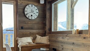 Une pièce chaleureuse avec un grand mur en bois, une horloge ronde, un canapé, un fauteuil et une fenêtre donnant sur les montagnes.