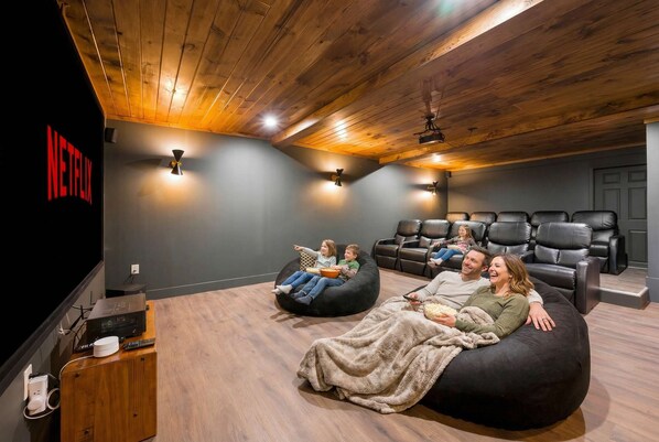 A cozy home theater with a wooden ceiling, a Netflix logo on the wall, and a seating area with bean bags and a couch.