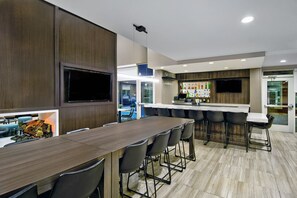 A modern kitchen with a long dining table, bar stools, and a flat-screen TV mounted on the wall. - Residence Inn by Marriott Reading (Wyomissing)