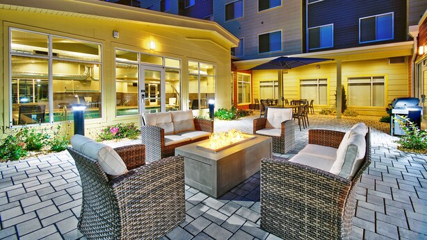 An outdoor patio area with wicker furniture, a fire feature, and a view of the building's interior. - Residence Inn by Marriott Reading (Wyomissing)