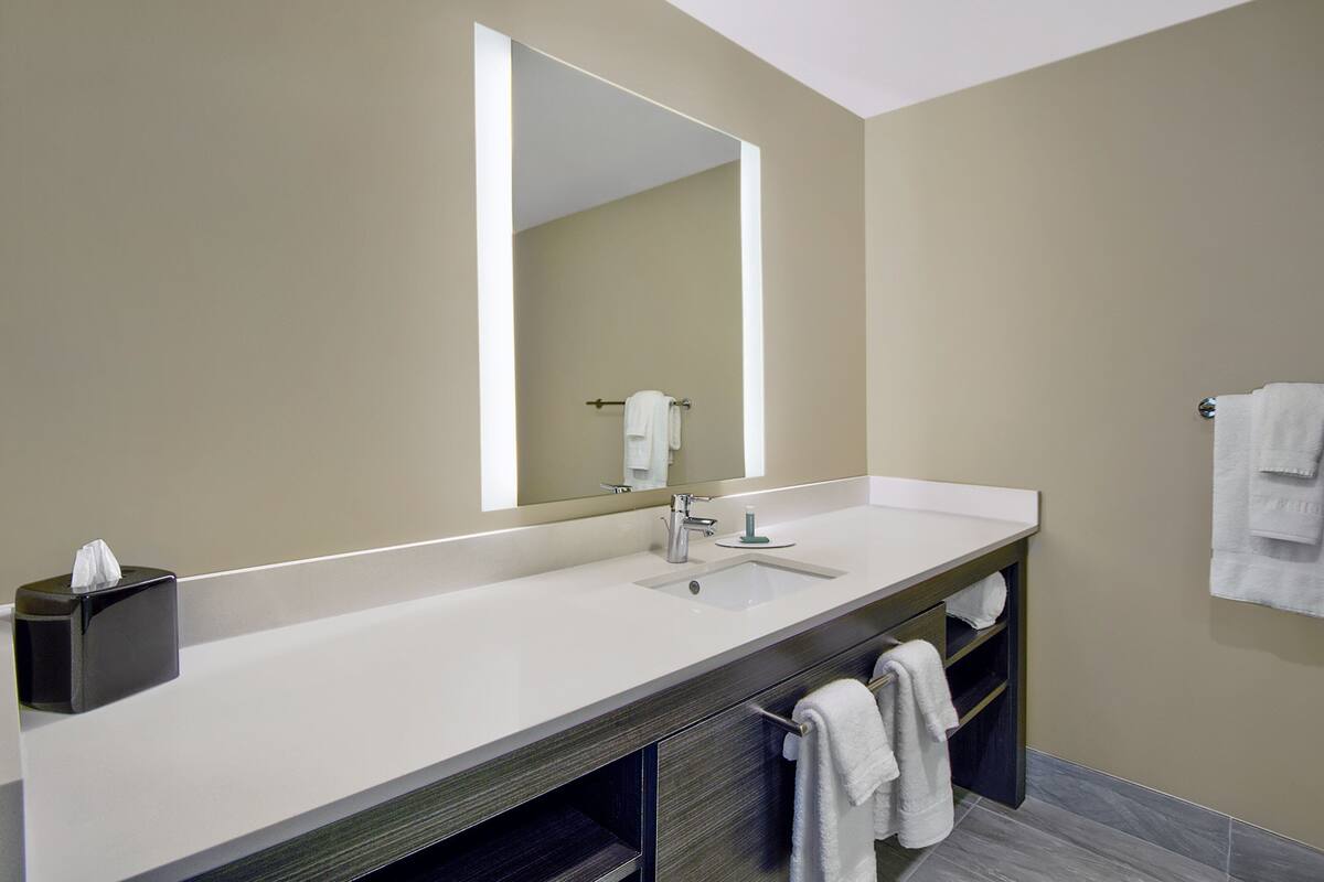 A modern bathroom with a large mirror, a white sink, and a towel rack.