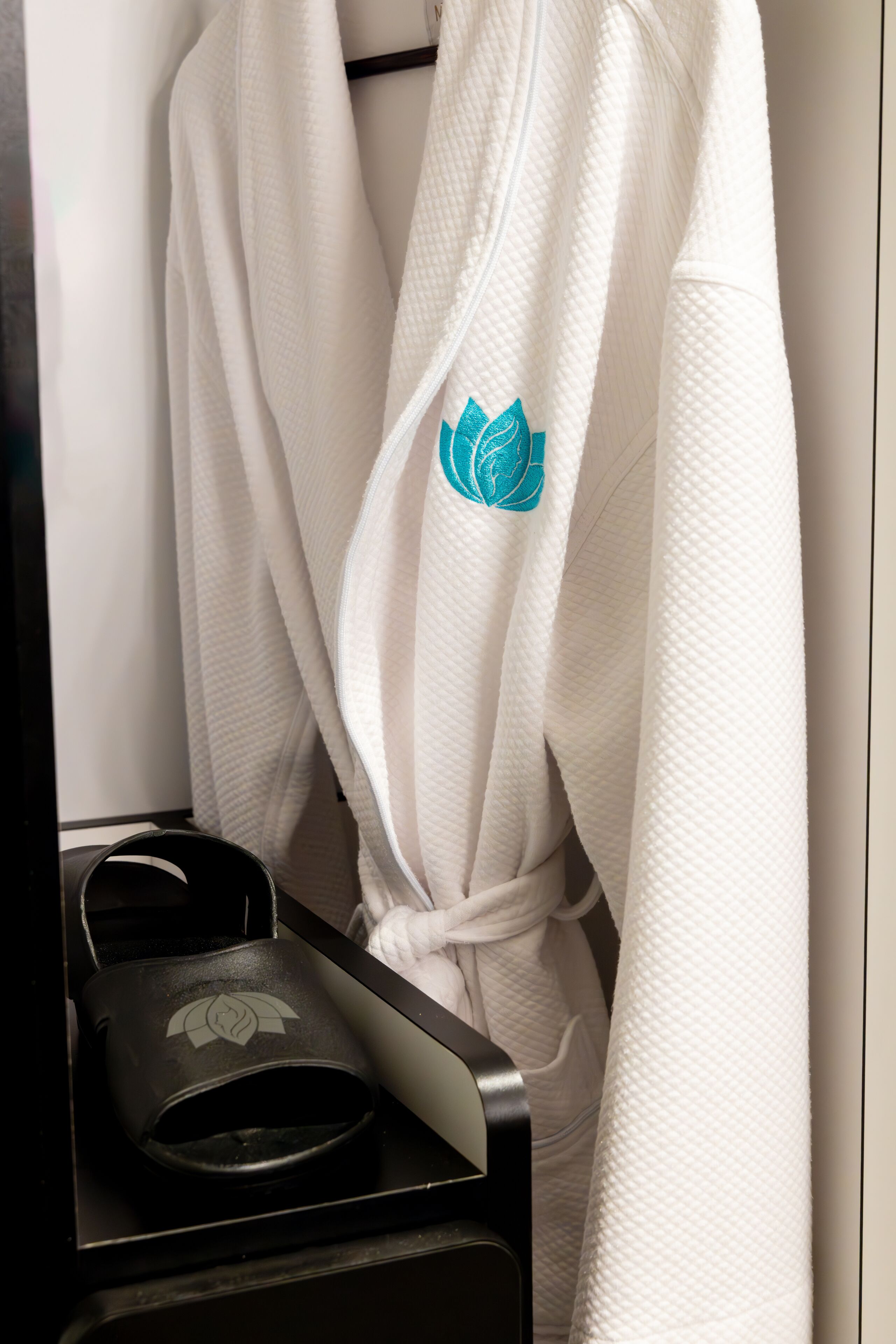 Une robe blanche ornée de motifs de feuilles bleues est suspendue à un porte-serviettes noir.