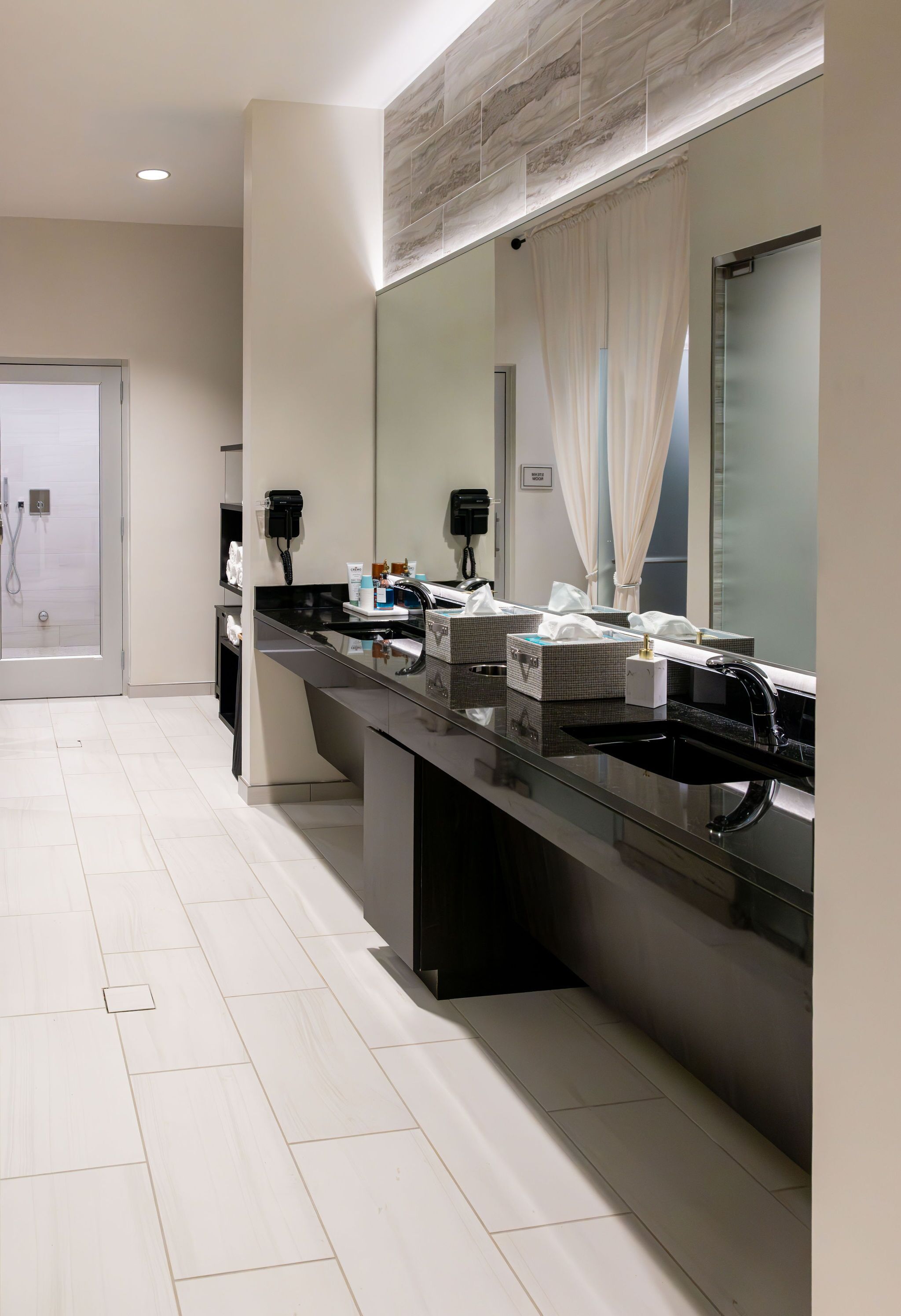 Un baño moderno con un espejo grande, un lavabo negro y una zona de ducha.