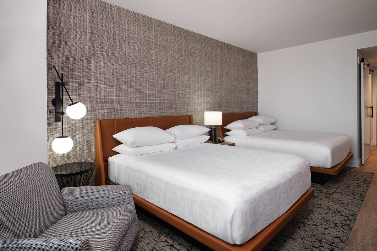 A hotel room with a large bed, a smaller bed, a sofa, a round table, and a wall-mounted lamp.