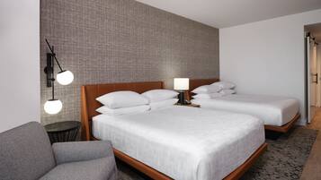 Una habitación de hotel con una cama grande, una cama más pequeña, un sofá, una mesa redonda y una lámpara fijada a la pared.