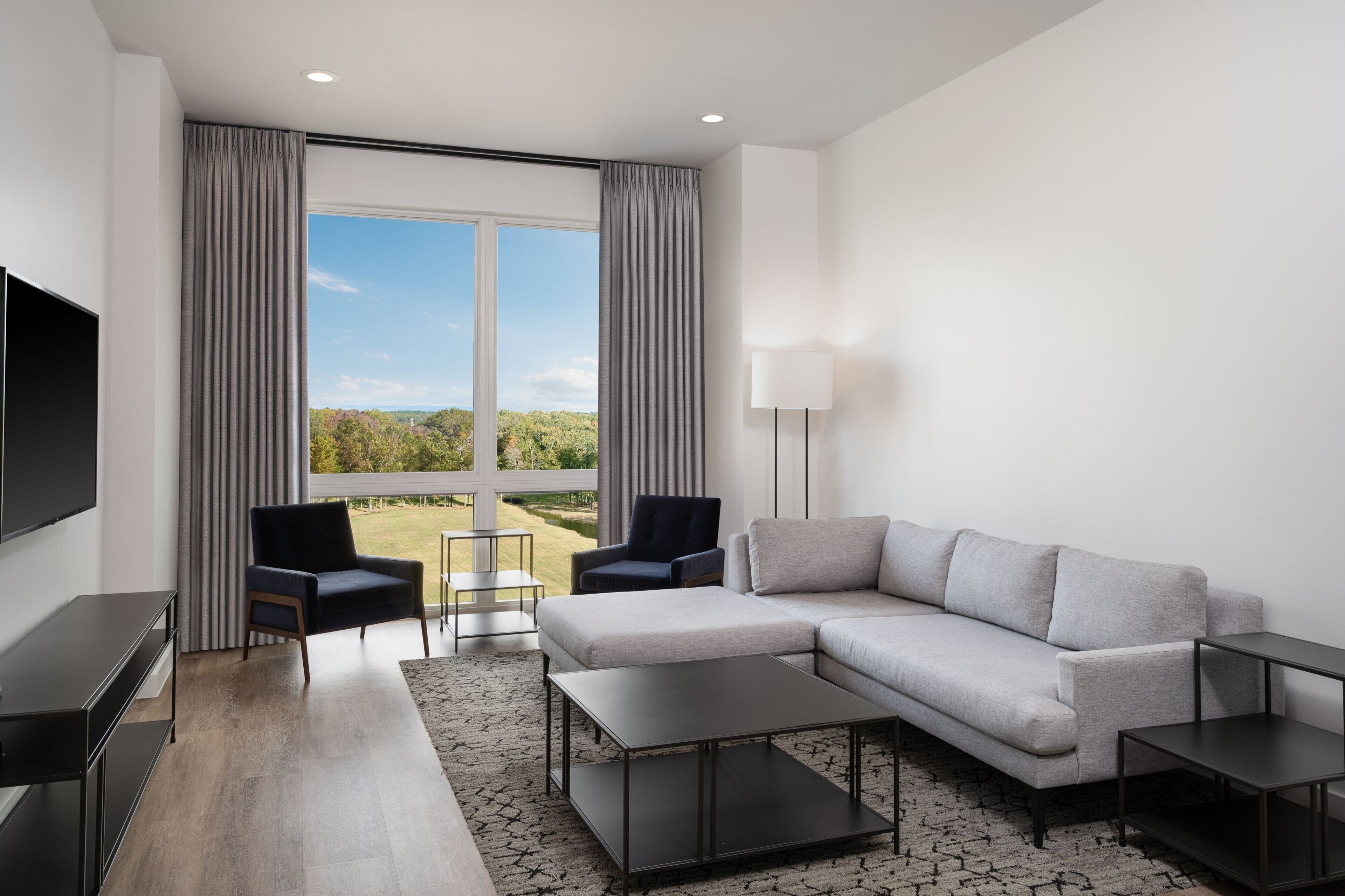 Una sala de estar moderna con un sofá modular, dos sillones, un televisor de pantalla plana y un amplio ventanal con vistas panorámicas.