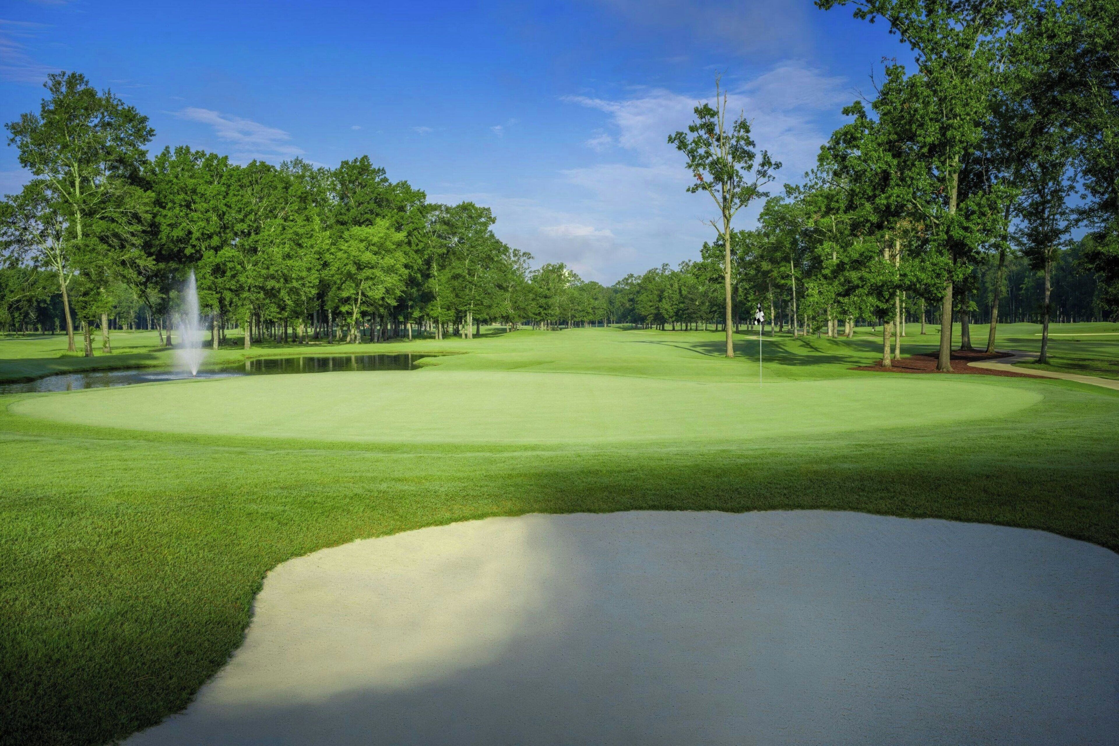 Campo de golf con un estanque, árboles y un búnker de arena.