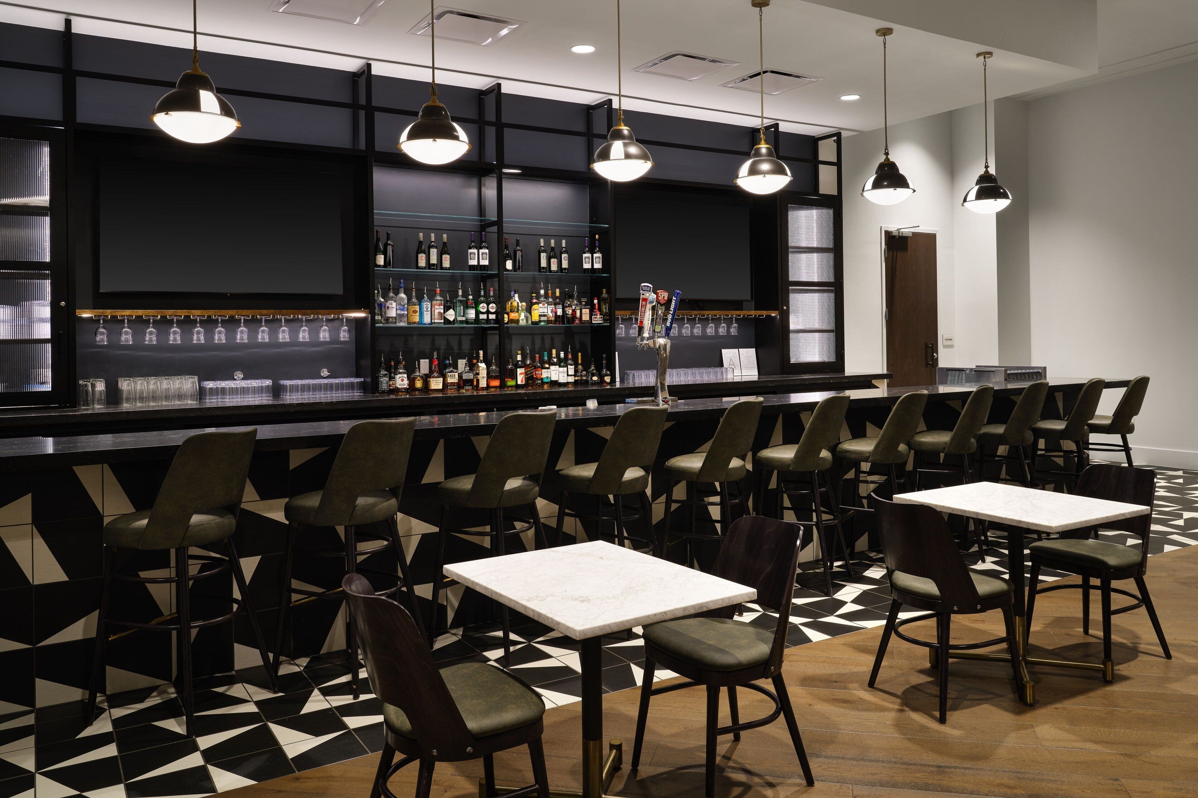 A bar area with multiple seating options, including bar stools and tables, and a variety of bottles on shelves.