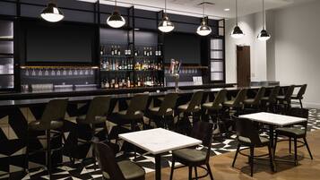 A bar area with multiple seating options, including bar stools and tables, and a variety of bottles on shelves.