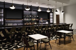 A bar area with multiple seating options, including bar stools and tables, and a variety of bottles on shelves.