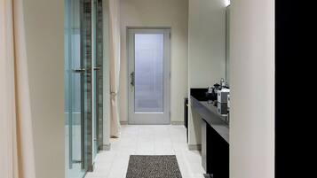 A narrow hallway with a glass door at the end, a black countertop with a mirror, and a patterned rug on the floor.