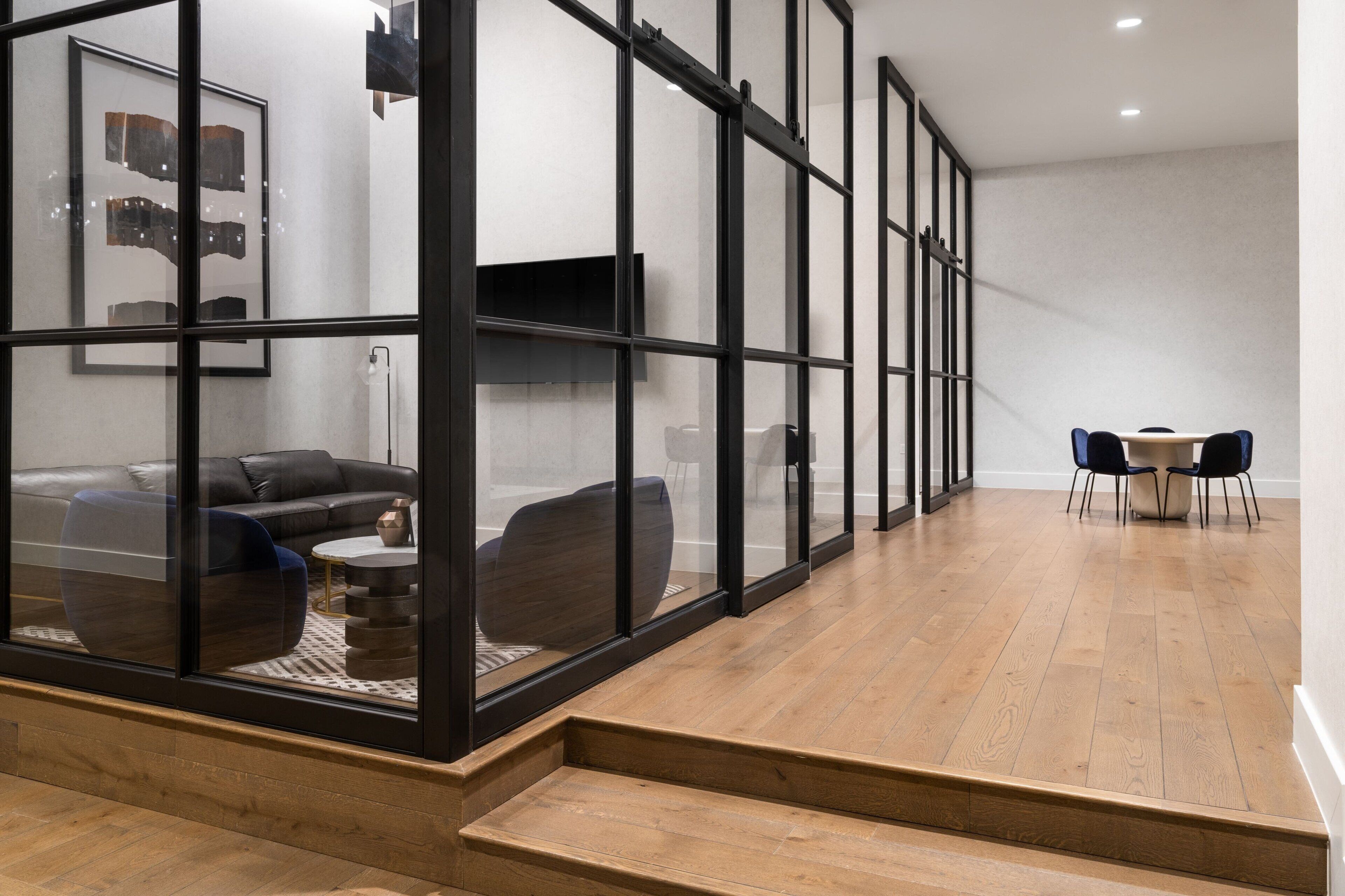 Una sala de estar moderna con un separador de vidrio, un sofá, una mesa de centro y un comedor con sillas.