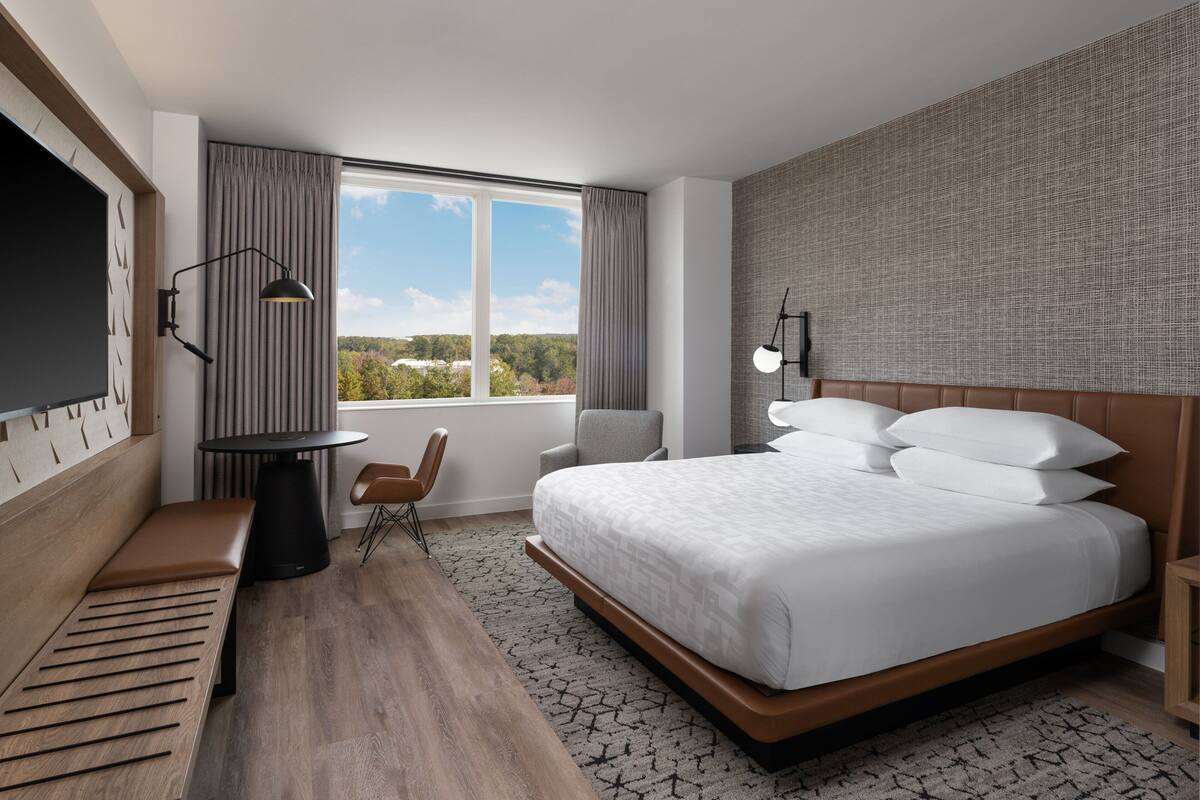 A modern hotel room with a large bed, a desk, a chair, and a TV.