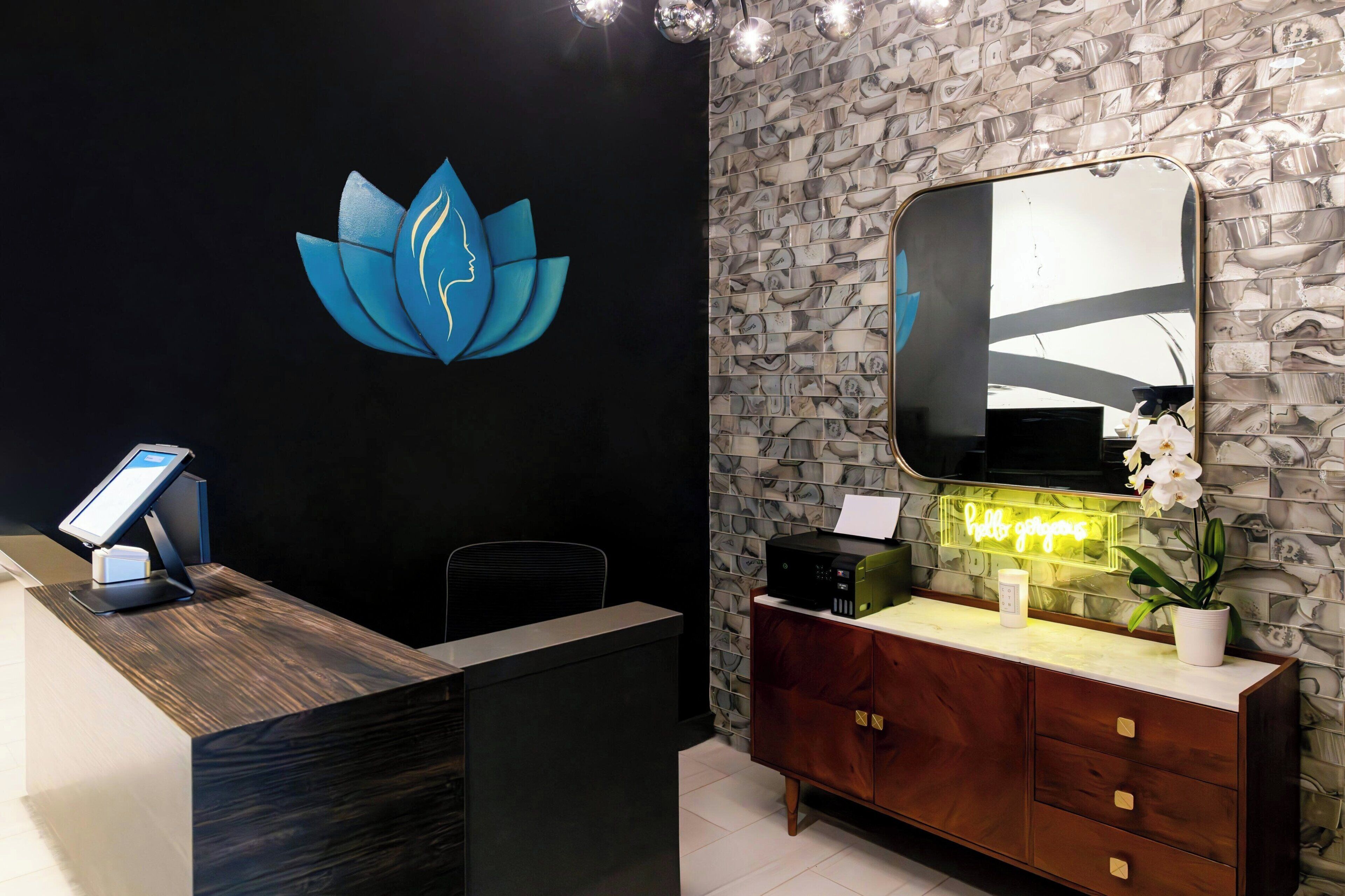 A reception desk with a digital kiosk, a neon sign, a mirror, and a potted plant.