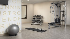 Un gimnasio con equipo de ejercicio, un televisor montado en la pared y un espejo.