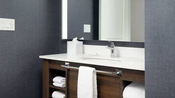Un baño moderno con un espejo grande, lavamanos blanco y barras para toallas.
