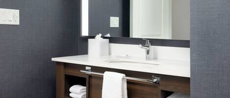 A modern bathroom with a large mirror, white sink, and towel racks.