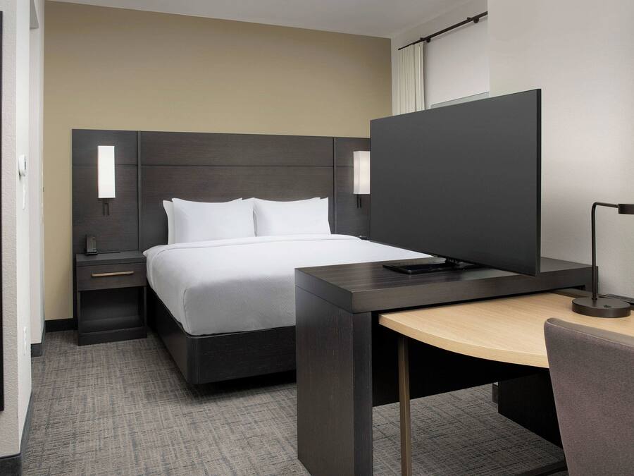 Ein modernes Hotelzimmer mit Bett, Nachttisch, Schreibtisch, Stuhl und Fernseher.