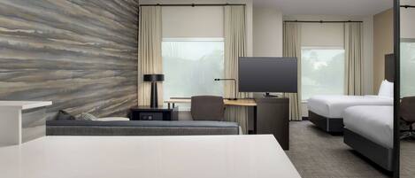A modern hotel room with a large bed, a desk, a chair, a TV, and a sofa.