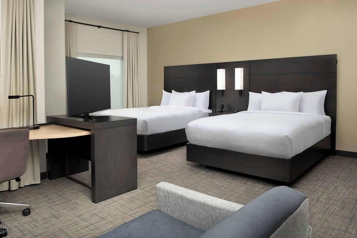 A hotel room with two beds, a desk, and a chair.