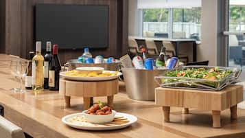 A well-organized buffet table with various food items, a selection of wine bottles, and a television in the background.