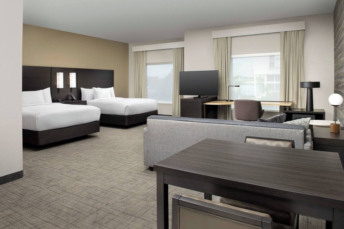 A hotel room with two beds, a desk with a computer, a TV, and a sofa.