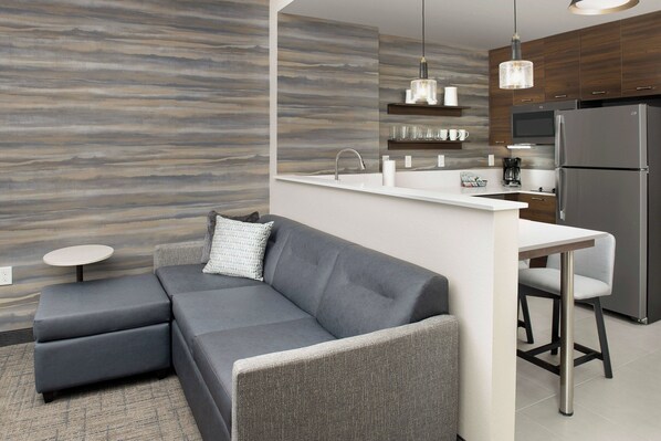 A modern kitchen with a grey sofa, a small round table, and a built-in island with a sink.