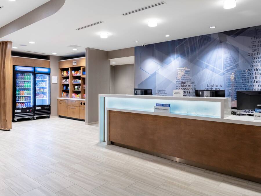 En modern hotellobby med en receptionsdisk, ett kylskåp för drycker och en välfylld snackbar.