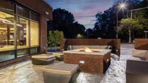An outdoor patio with a fire feature, seating, and a building with large windows. - SpringHill Suites by Marriott Durham City View (Durham)
