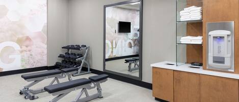 A gym with weight benches, dumbbells, and a mirror.