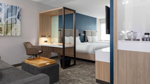 A modern hotel room with a bed, a desk, a chair, a small seating area, and a kitchenette. - SpringHill Suites by Marriott Durham City View (Durham)