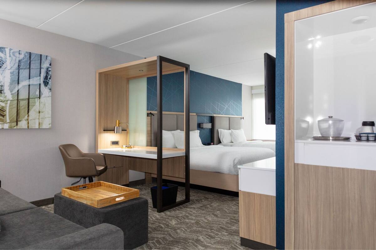 Une chambre d’hôtel moderne équipée d’un lit, d’un bureau, d’une chaise, d’un petit coin salon et d’une kitchenette.