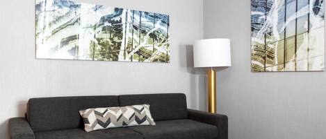 Una sala de estar moderna con un sofá gris, un cojín estampado y dos cuadros abstractos en la pared.