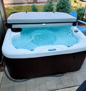 Un bain à remous doté d’une structure extérieure en bois, d’un panneau de commande et d’un tuyau qui y est raccordé.