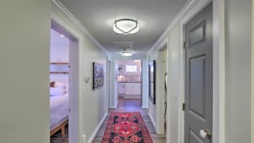 A hallway with a patterned rug, a bed, a kitchen, and a door.