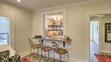 A kitchen with a bar area, three bar stools, and a countertop with various kitchen items.