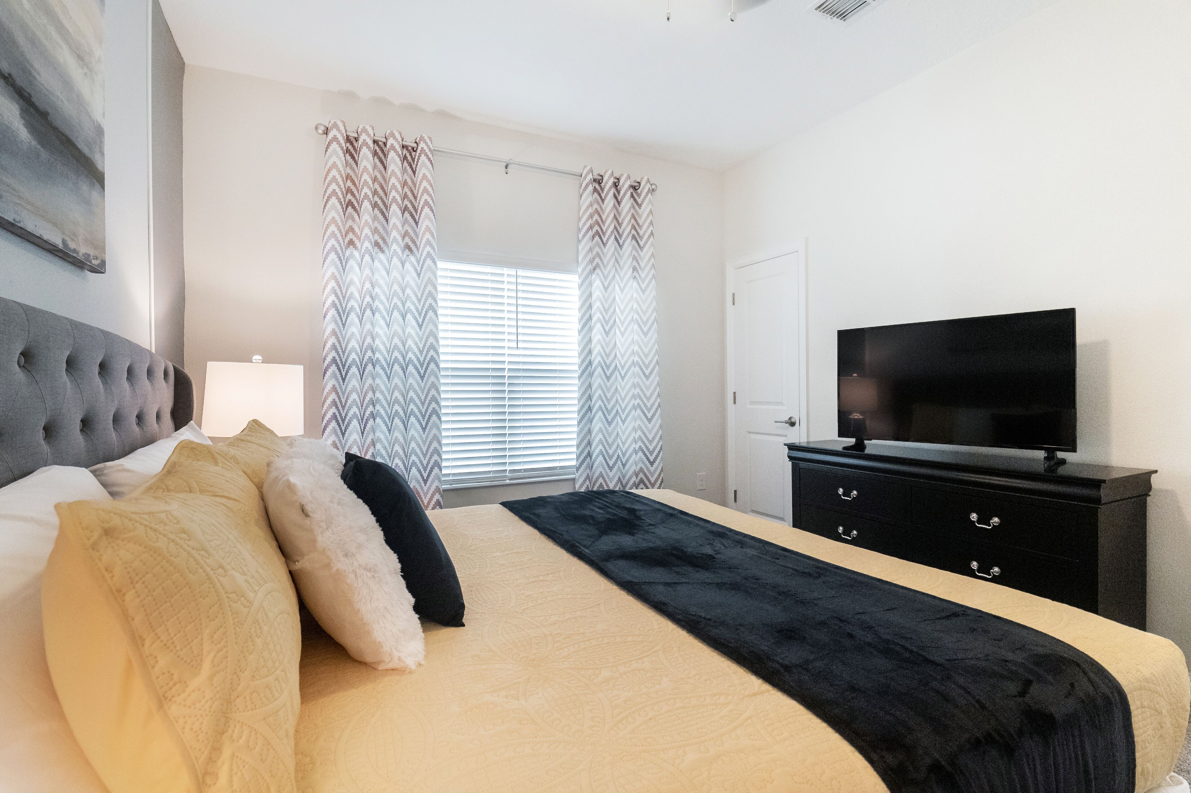 A bedroom with a bed, a television, a dresser, and a window with curtains.