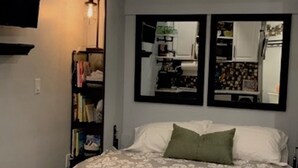 Un dormitorio con cama, estantería, escritorio y espejo.