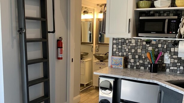 Cocina compacta con microondas integrado, refrigerador y salpicadero de piedra.