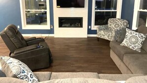 A living room with a fireplace, a television mounted above it, and two windows. - Country living with a pool, fire pit & family-friendly! (Fond du Lac)