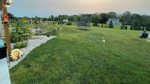 A grassy backyard with a trampoline, a bird feeder, and a garden with sunflowers. - Country living with a pool, fire pit & family-friendly! (Fond du Lac)