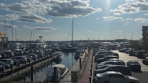 A marina with boats docked, a parking area with cars, and a clear sky with sunlight.