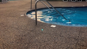 A swimming pool with a metal ladder, lounge chairs, and umbrellas.