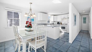 A modern kitchen with white cabinetry, a glass dining table, and a blue-tiled floor. - Beach Front! (Long Beach)